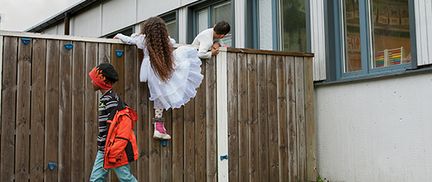 Barn som klättrar över ett staket i klänning. Foto: Lo Birgersson