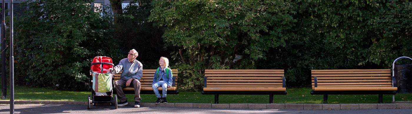 En vuxen och ett barn sitter på en bänk vid en utegård.