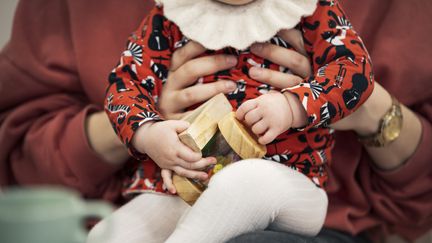 Ett barn sitter i knät på en vuxen och håller i två träleksaker.