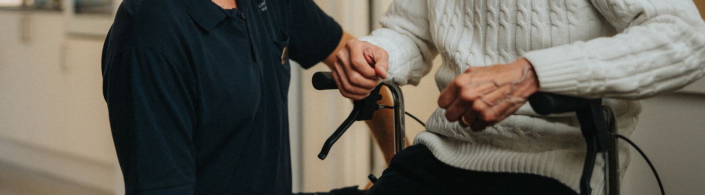 En fysioterapeut visar en senior hur han ska använda en rullator.
