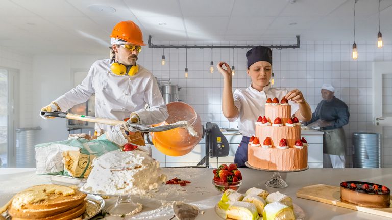Två bagare står och gör varsin tårta. Bagaren till vänster har kläder som passar för en byggarbetsplats och lastar mjöl i en cementblandare.